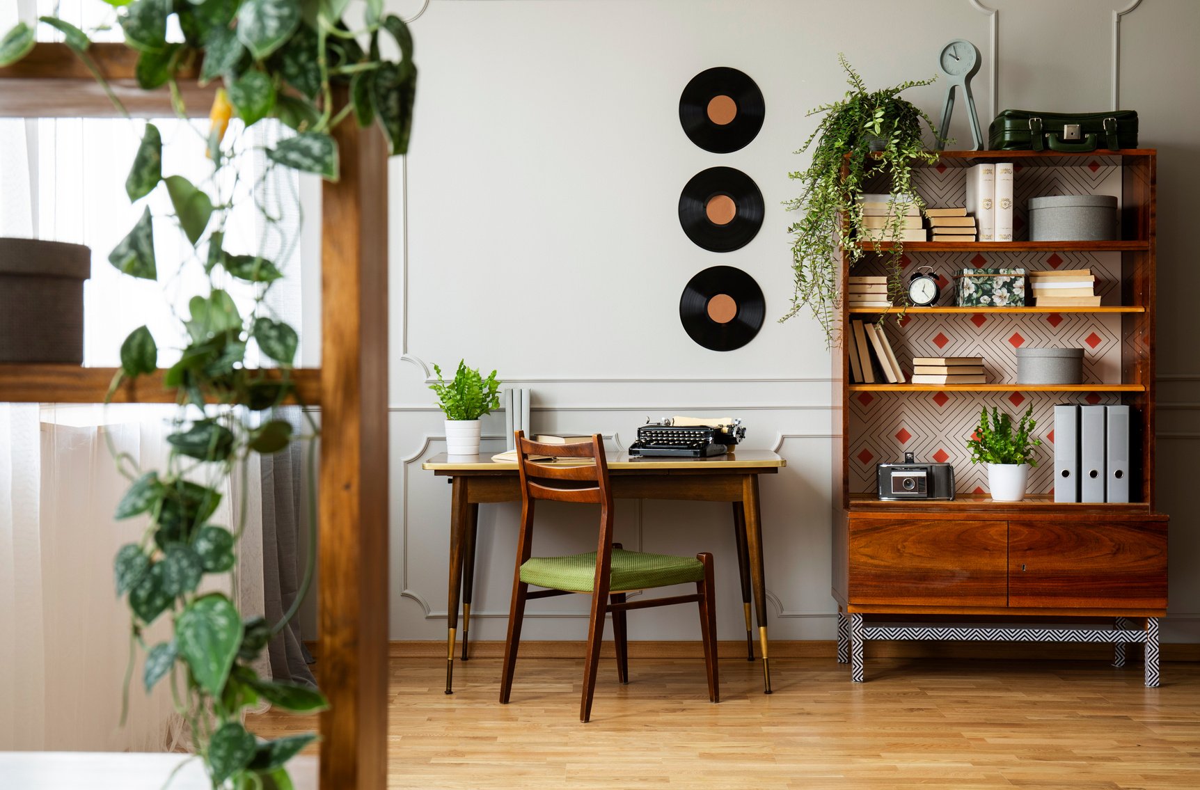 Black retro typewriter on a unique wooden desk, a mid-century modern chair and a renovated bookcase in a hipster home office interior. Real photo.